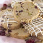 Cranberry pistachio shortbread cookies on a pink plate, some with a drizzle of white chocolate.