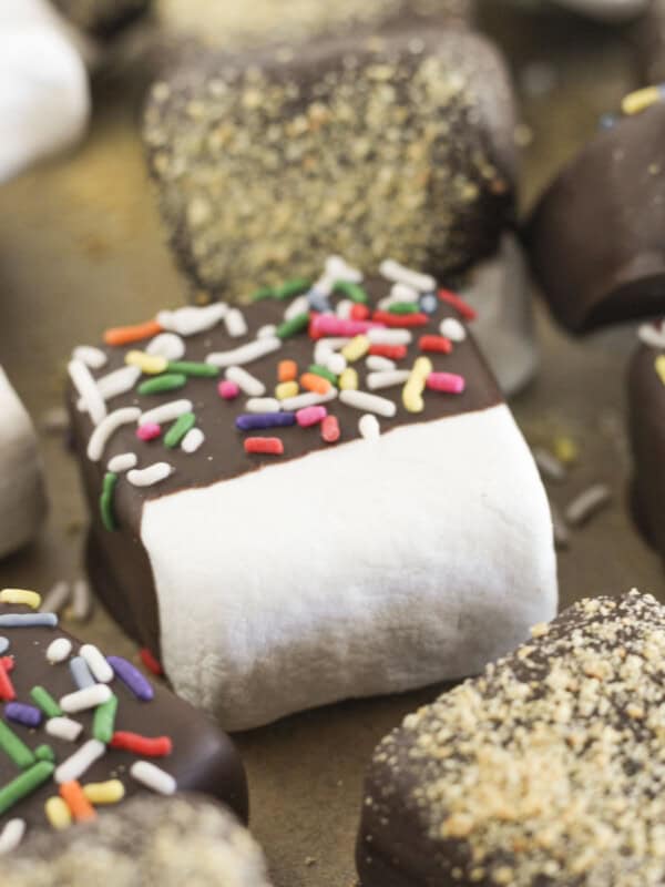 Chocolate covered marshmallows with sprinkles drying on a cookie sheet.