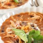 Two bowls of chicken enchilada soup with toppings.
