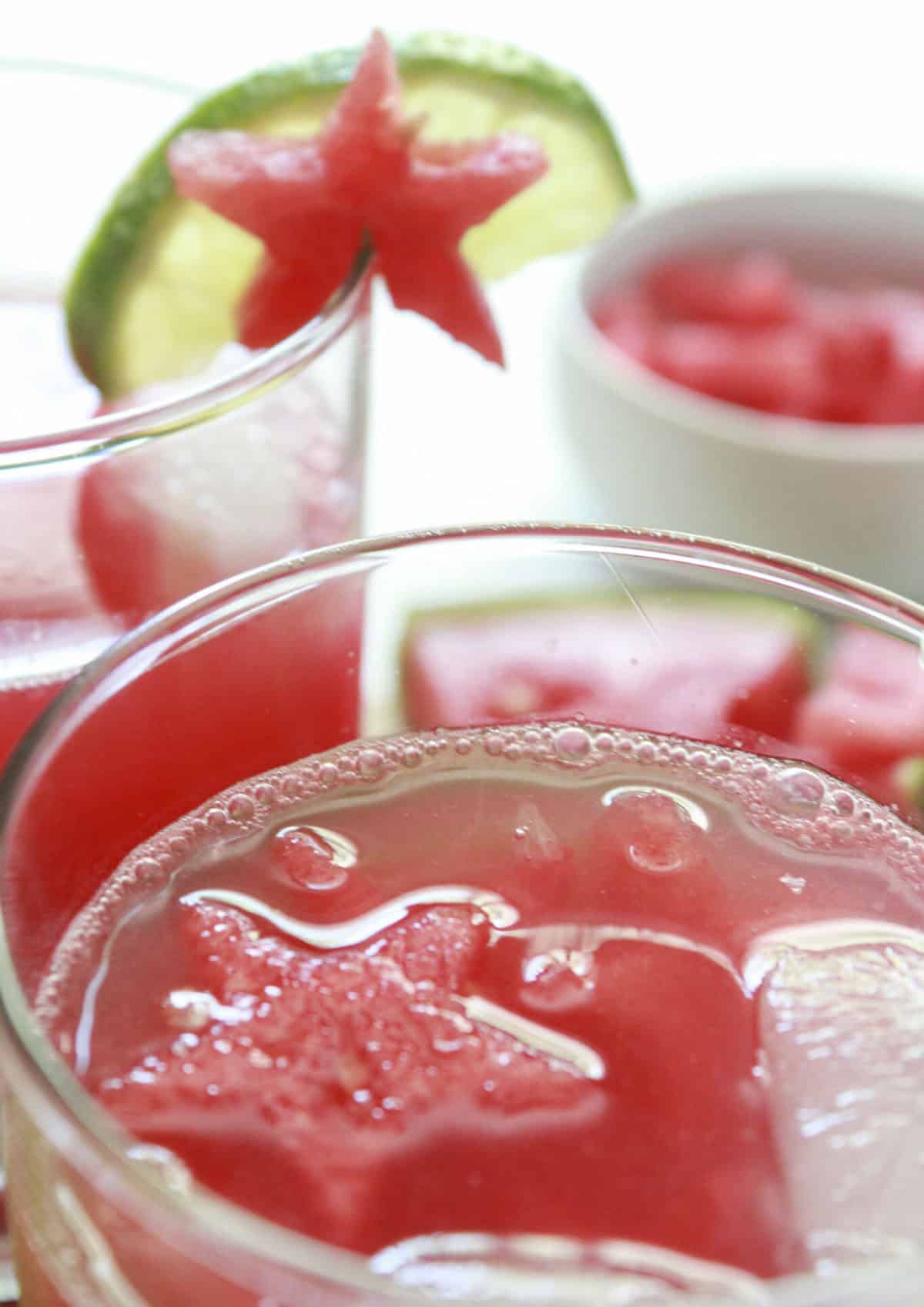 Watermelon limeade is served in glasses with garnishes of lime and watermelon.