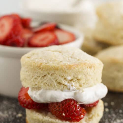 Sweet biscuits on a baking tray with whipped cream and strawberries.