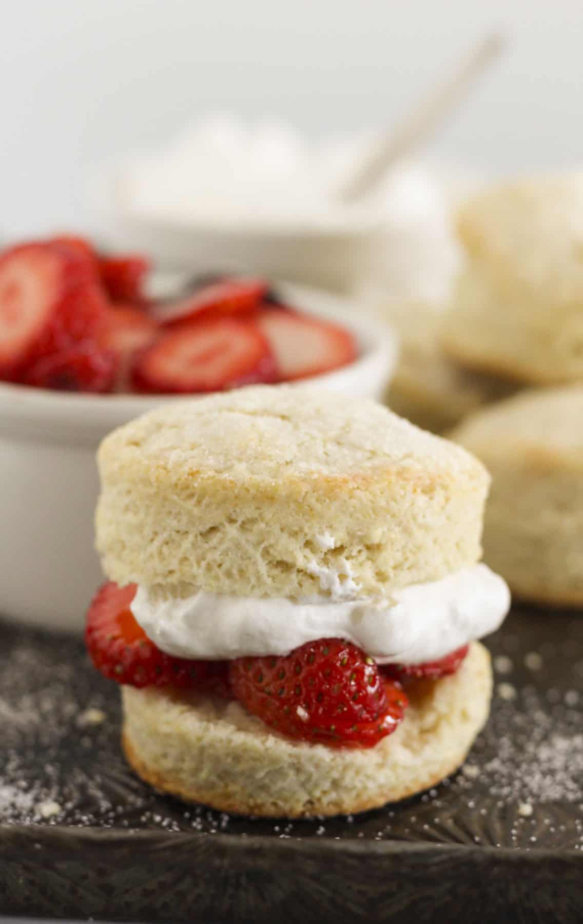 Baked sweet biscuits on a tray with sugared strawberries and whipped cream.