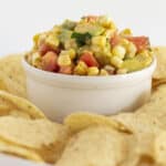 Corn and avocado salsa served in a white bowl with corn chips.