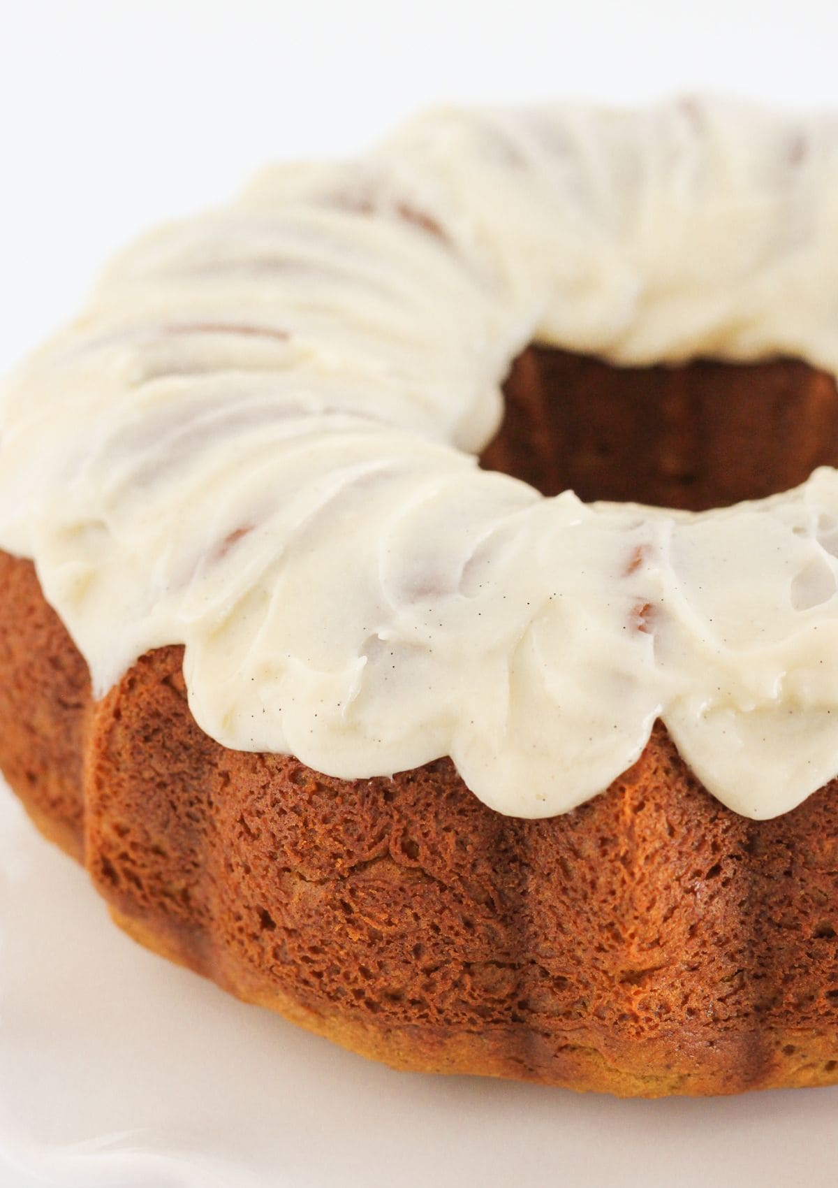 Adding cream cheese frosting to the top of a baked pumpkin spice cake.