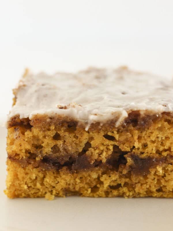 A slice of cinnamon roll pumpkin cake with glaze on top.