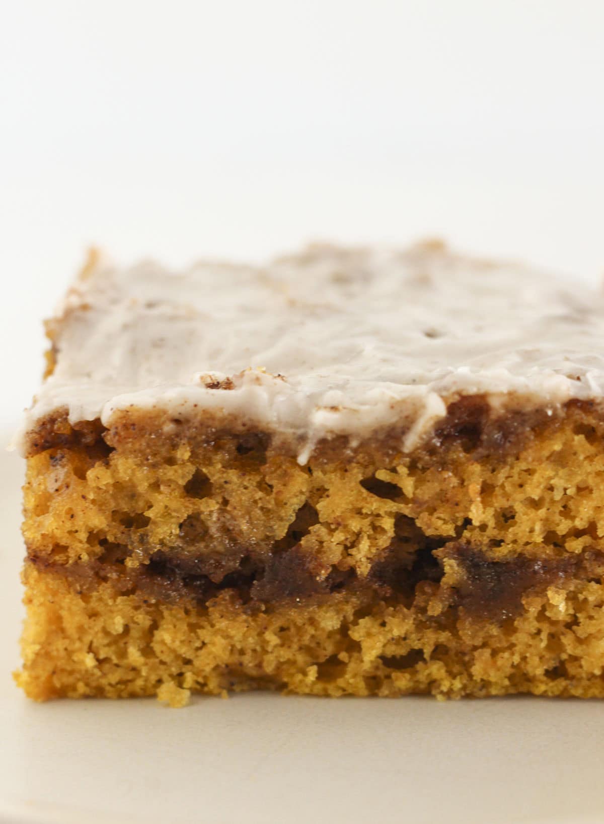 A slice of cinnamon roll pumpkin cake with glaze on top.