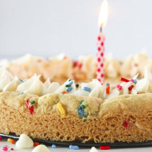 A birthday cookie cake with sprinkles and a candle.