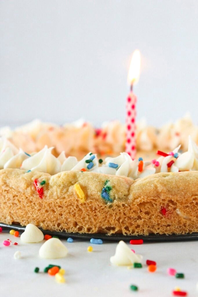 A birthday cookie cake with sprinkles and a candle.