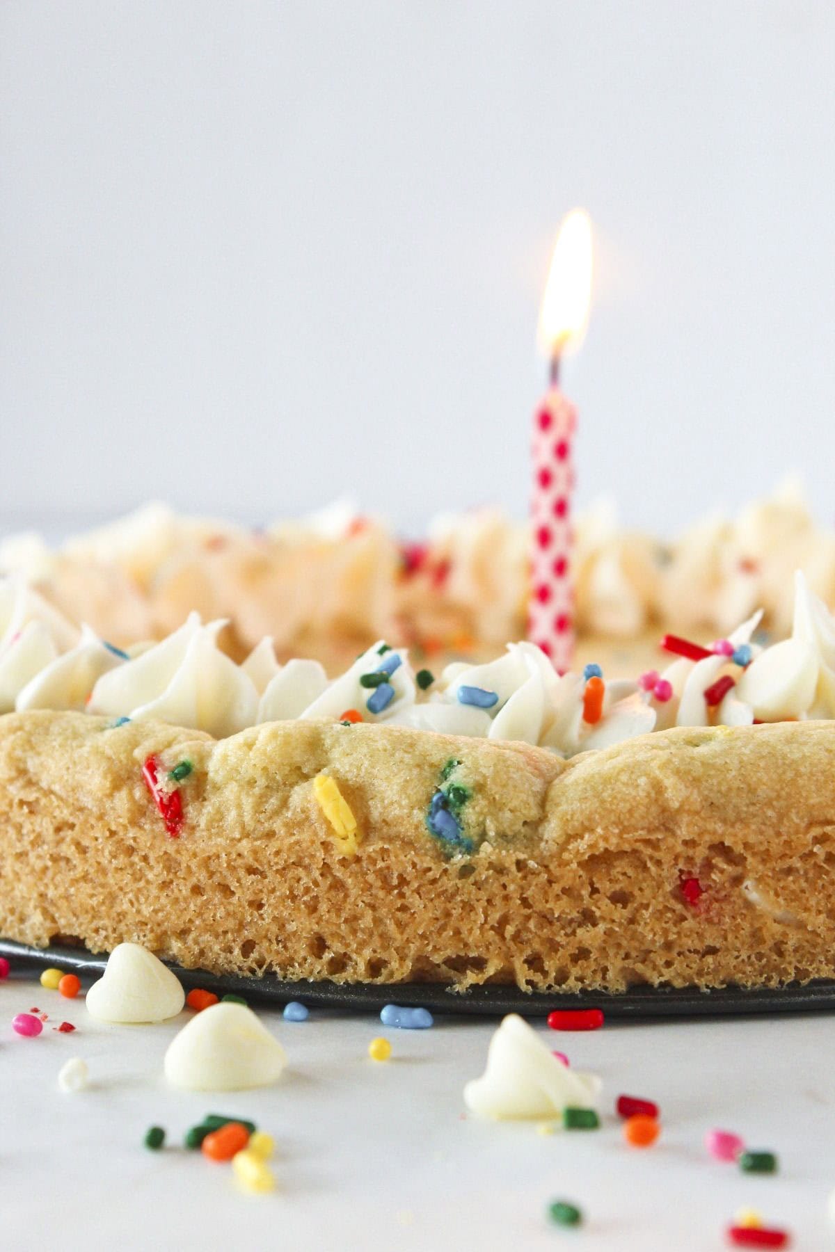 A birthday cookie cake with sprinkles and a candle.