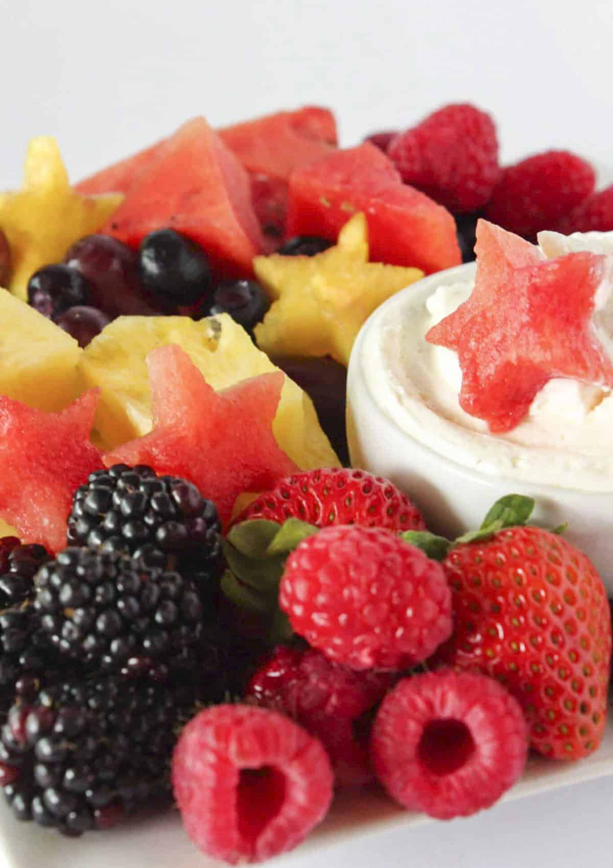 A festive fruit tray with fresh fruit, some cut into star shapes and cheesecake dip.