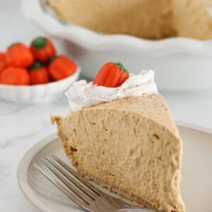 A slice of pumpkin mousse pie on a plate with whipped topping.