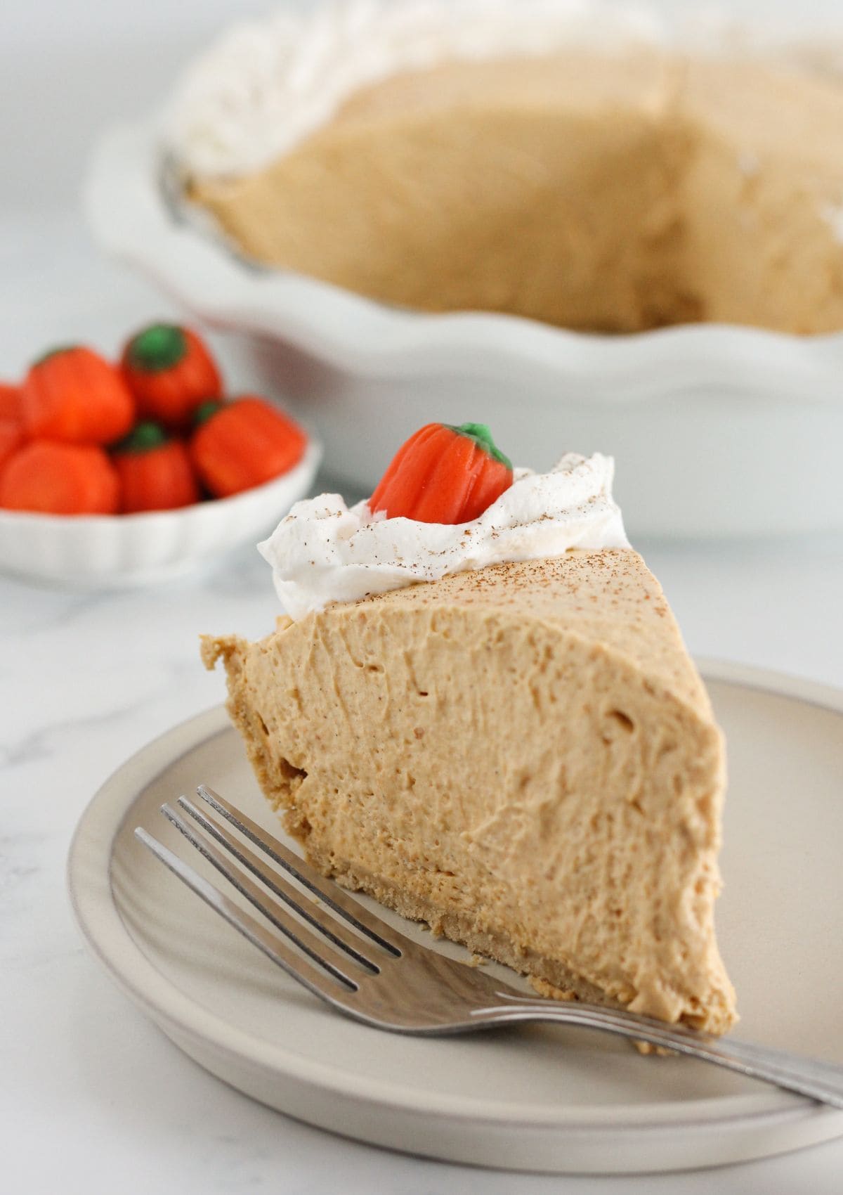 A slice of pumpkin mousse pie on a plate with whipped topping.