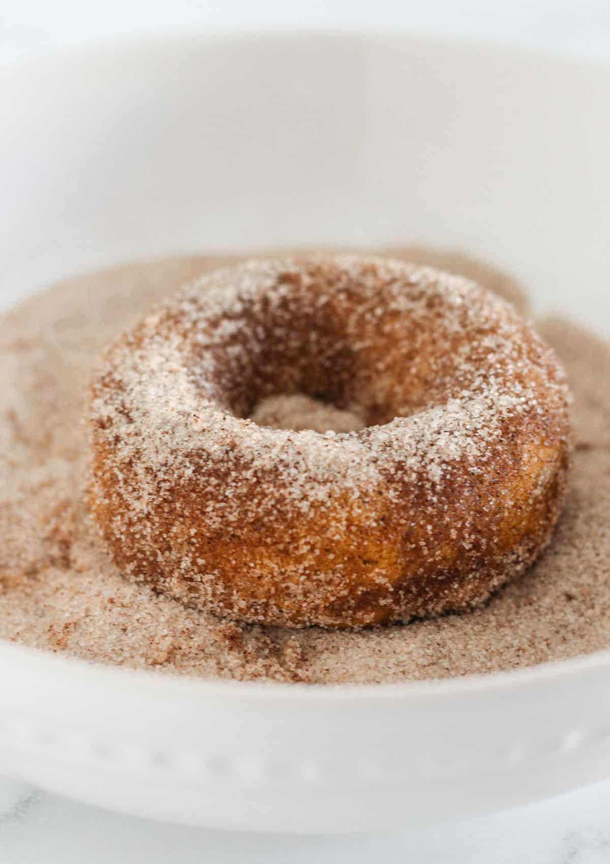 Rolling the buttered donuts in cinnamon sugar.