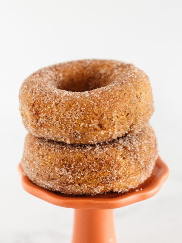Two pumpkin spice donuts on an orange cake plate.