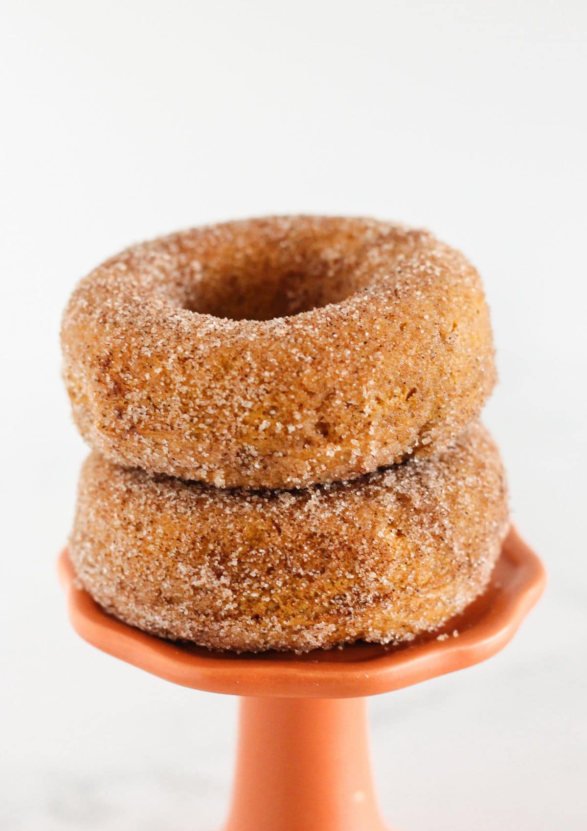 Two pumpkin spice donuts on an orange cake plate.