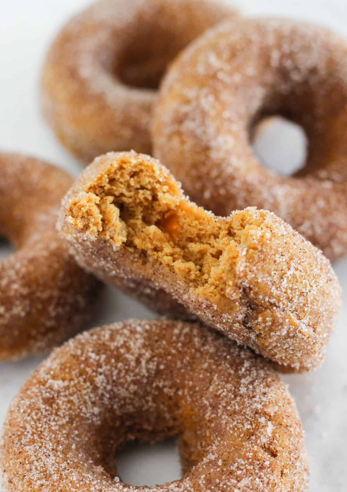 Pumpkin spice donuts on a tray with a bite taken from one.