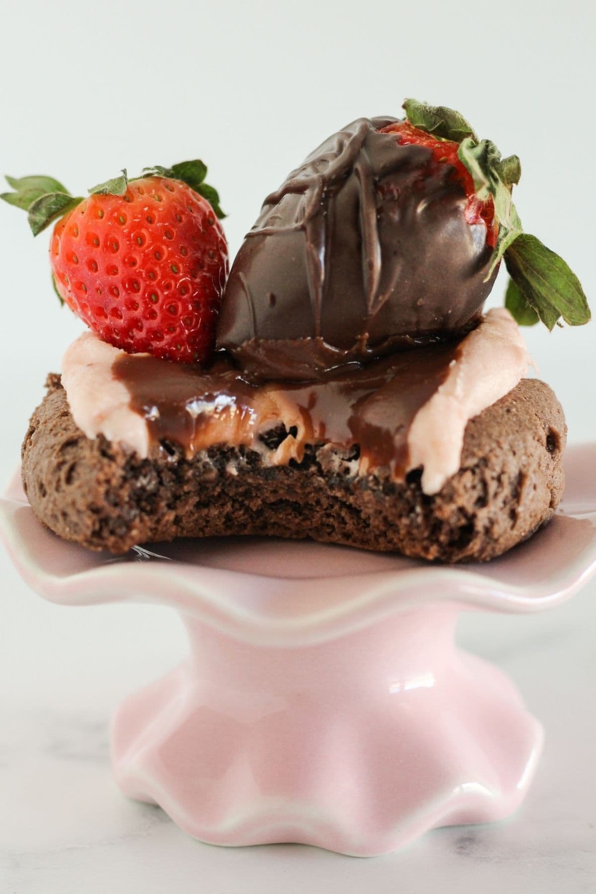 A single chocolate covered strawberry cookie with a bite taken.
