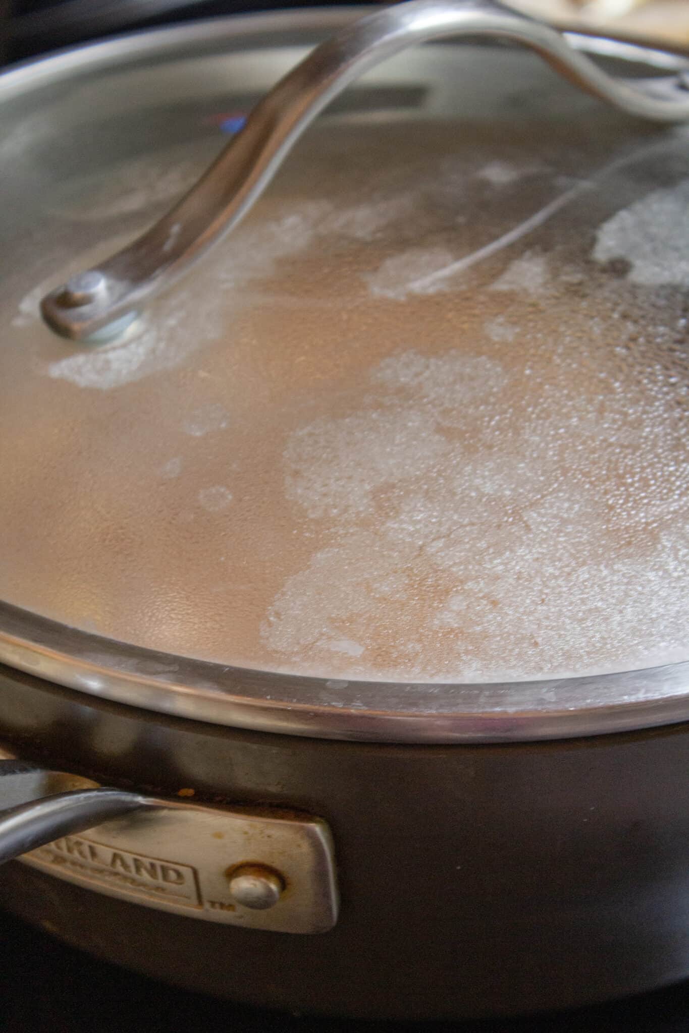 Adding the pasta and covering the skillet to allow it to cook.