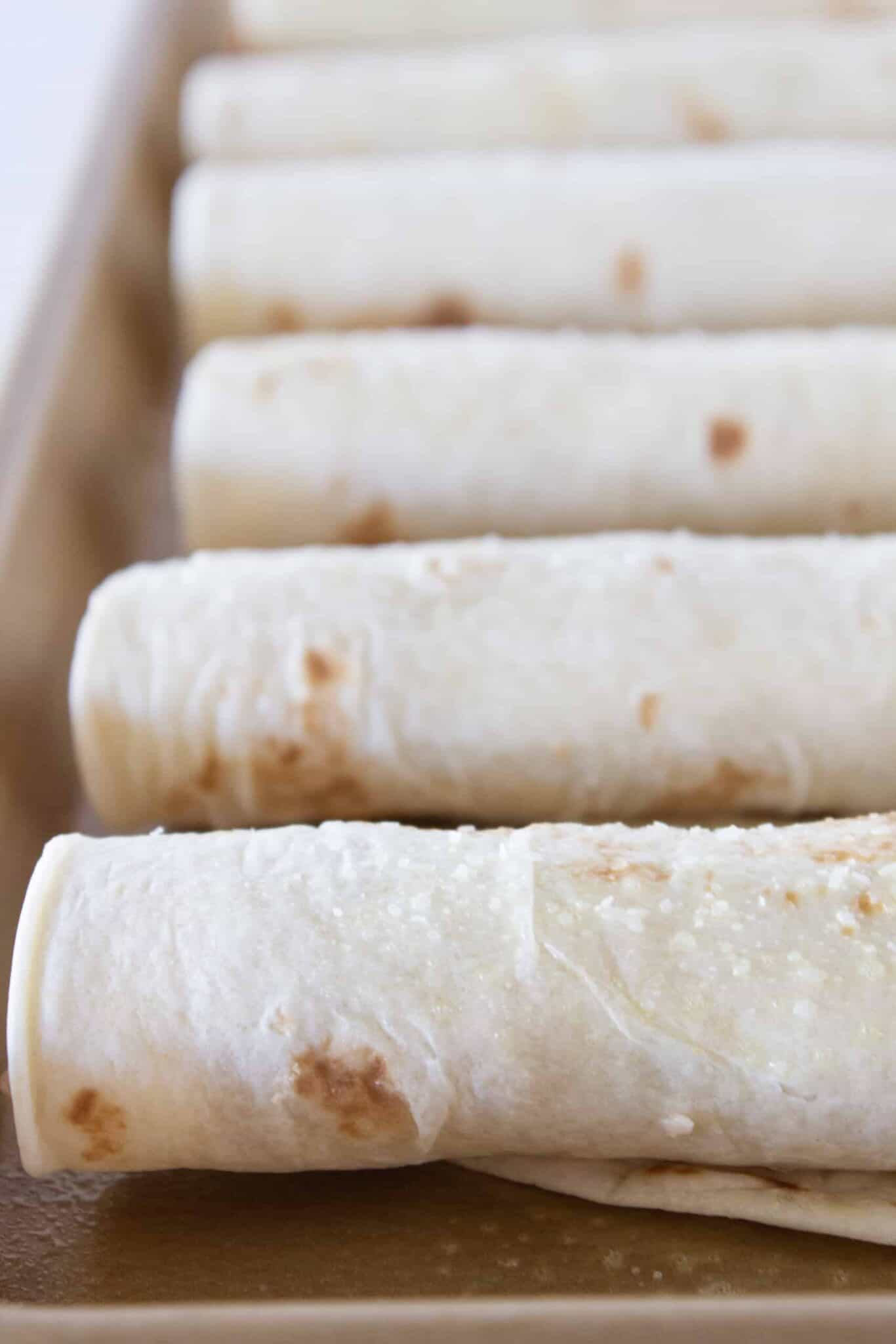 Placing the rolled taquitos onto a sheet pan so they are ready to bake.