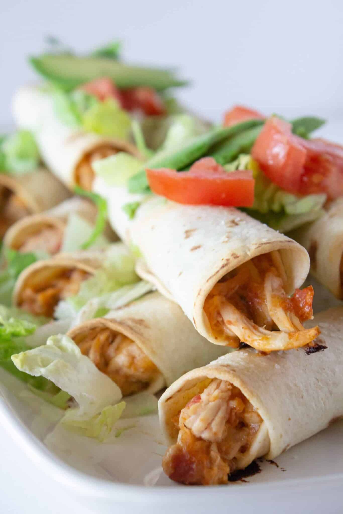 Chicken taquitos on a tray and being served with lettuce and tomato.