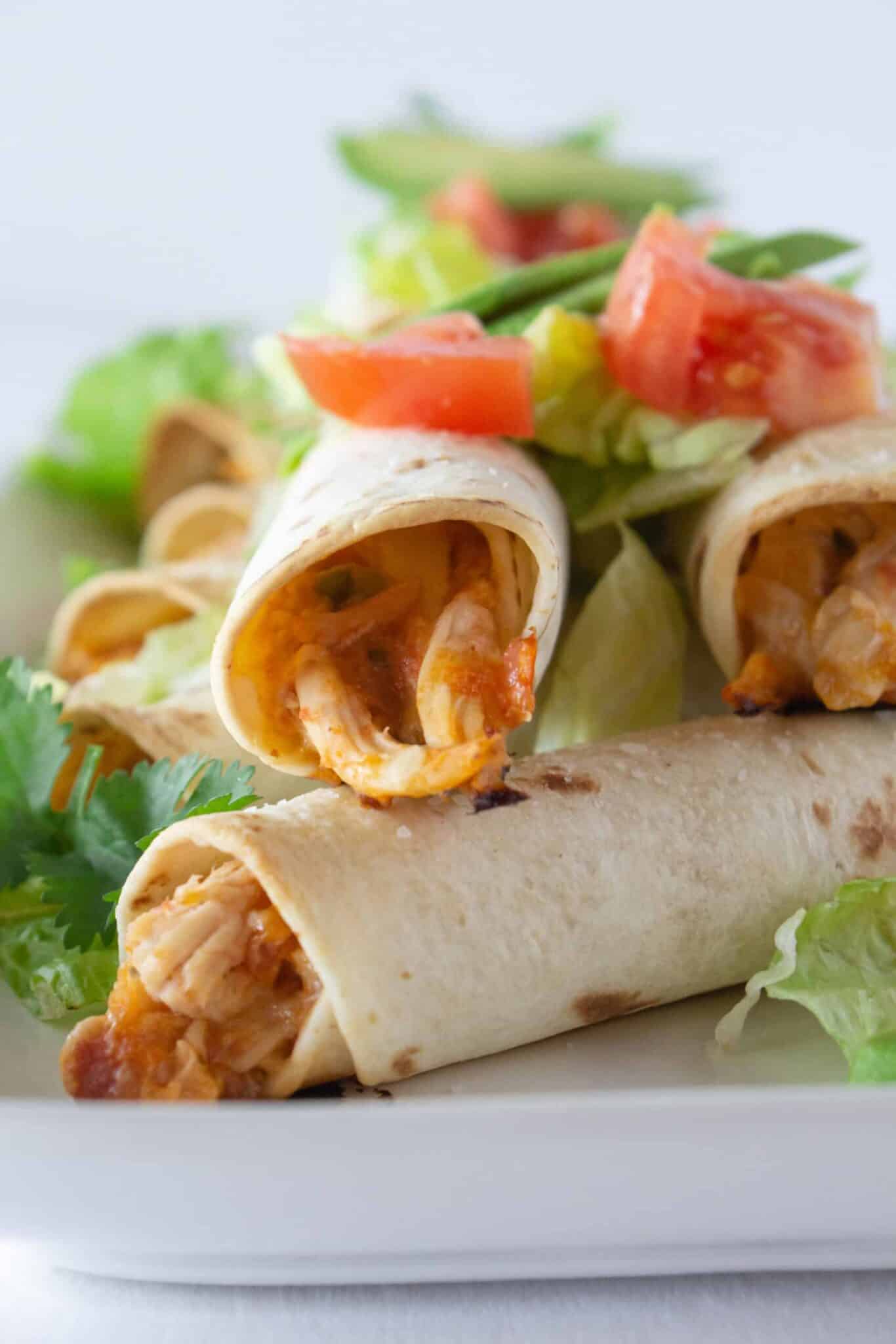 A tray of chicken taquitos with toppings on a table and ready to serve.