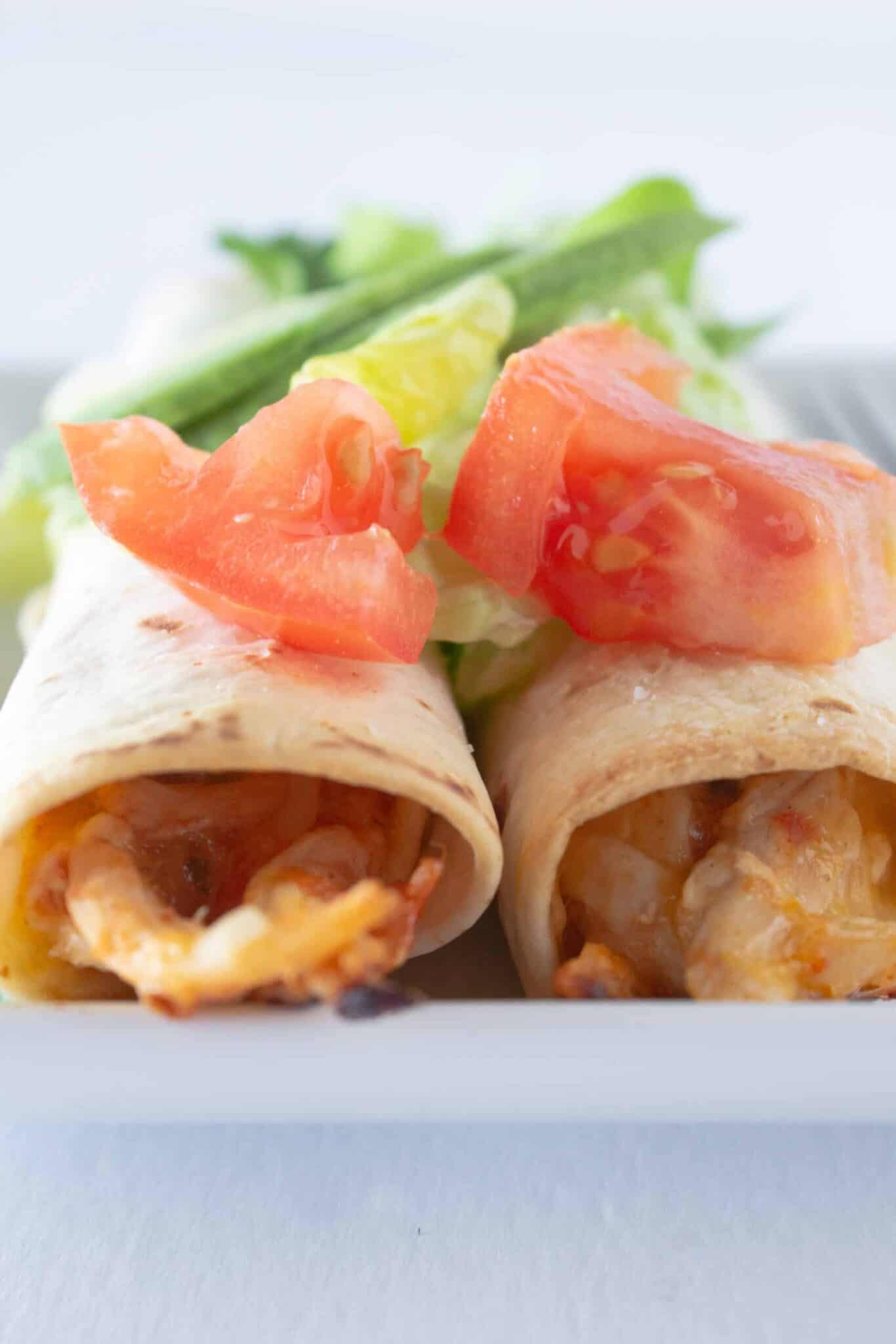 A serving of 5 ingredient chicken taquitos on a plate with tomato and avocado.