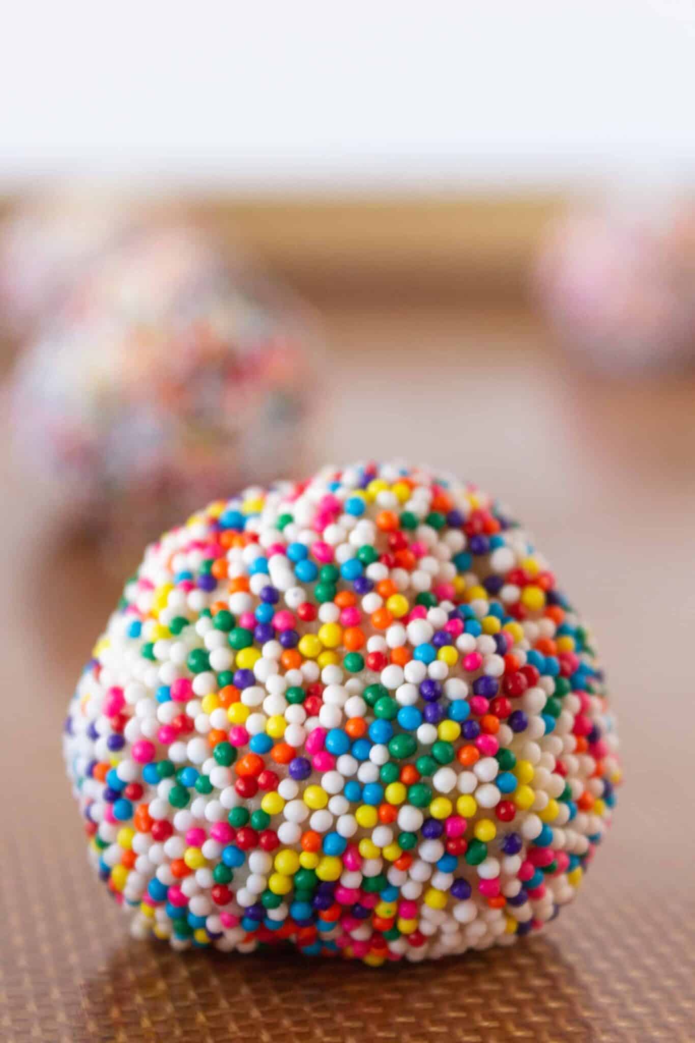 Rolling the cookie dough balls in sprinkles and placing on a baking sheet.