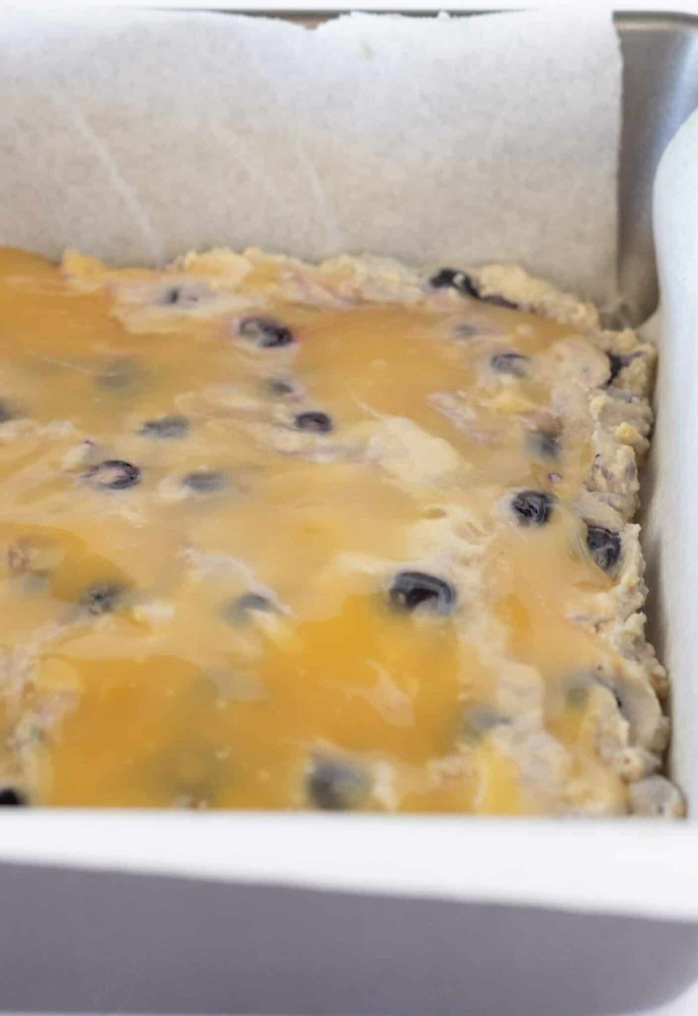 Adding the lemon blueberry crumb cake batter to the prepared pan and adding lemon curd to top.