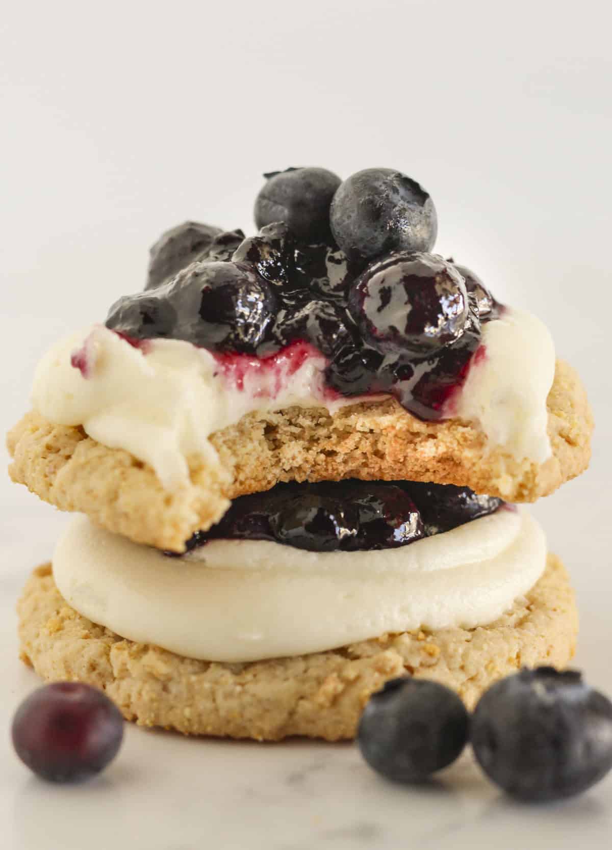 Two blueberry cheesecake cookies stacked on each other with a bite from the top cookie.