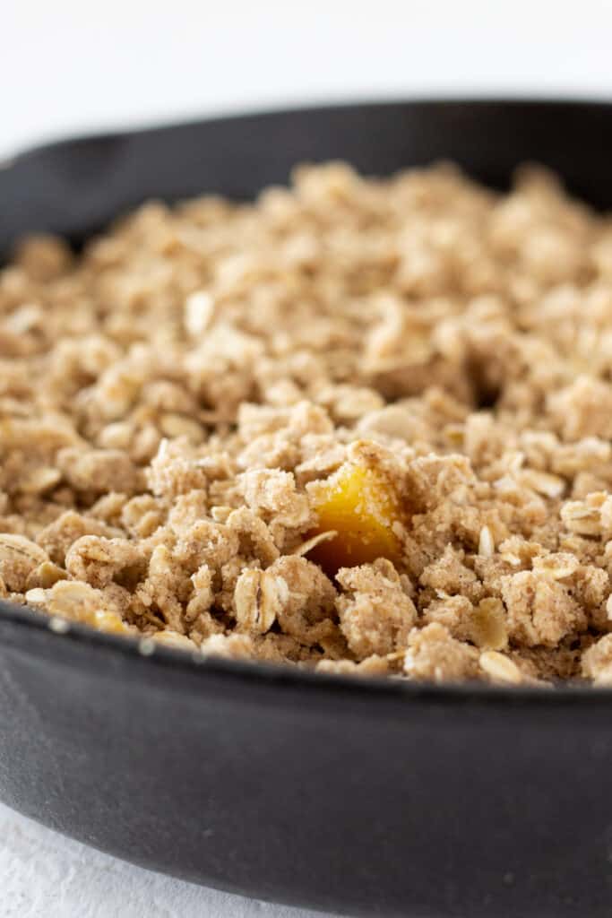 Unbaked peach crisp with canned peaches in a skillet.