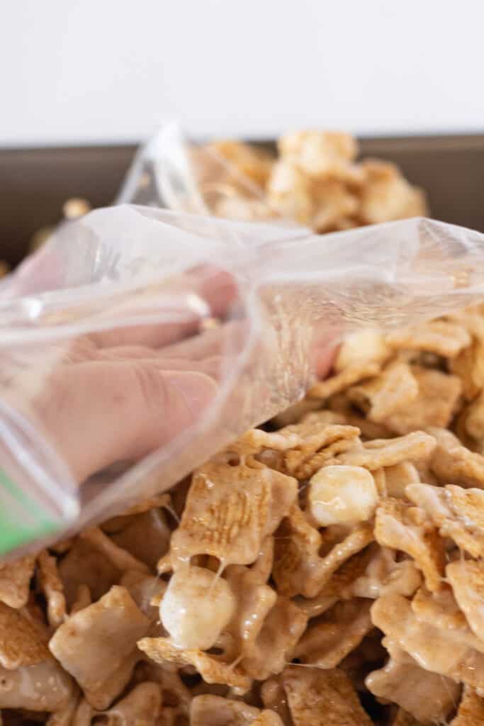 A hand covered in a plastic bag, pressing the cinnamon toast crunch dessert down into the pan.