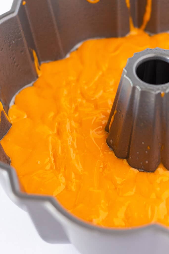 A layer of orange cake batter in a bundt pan.