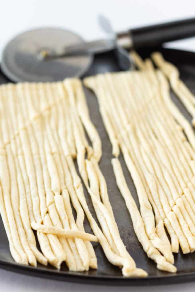 Long thin strips of crescent roll dough with a pizza cutter seen in the background.