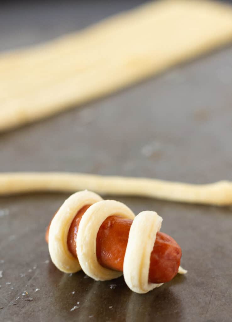 A miniature hot dog wrapped with one strip of crescent roll dough.