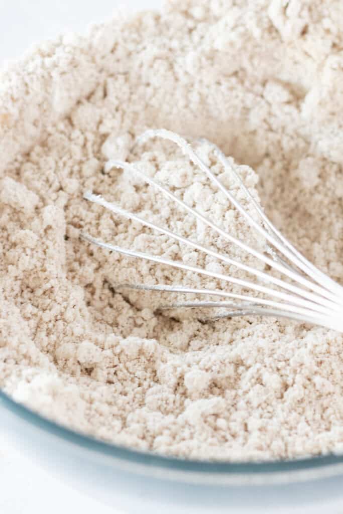 A whisk in a glass mixing bowl with Bisquick pancake mix and brown sugar.