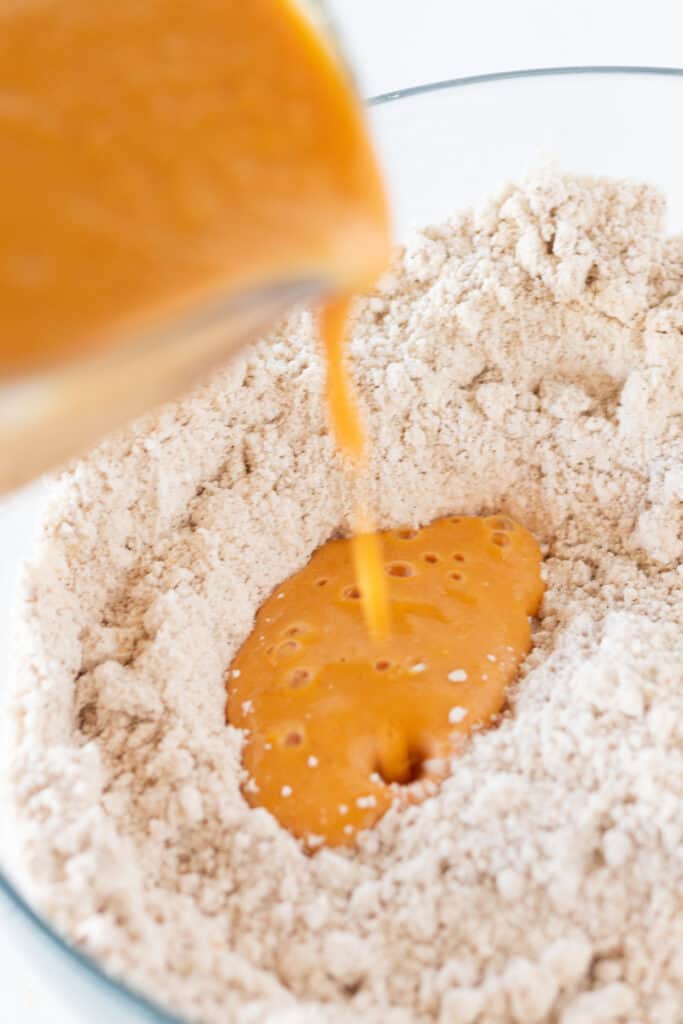 The wet pumpkin mixture being poured into the dry Bisquick mixture in a glass mixing bowl.