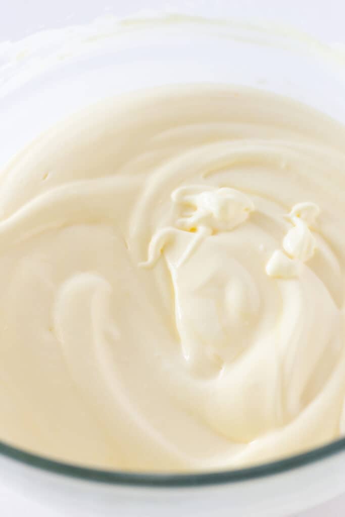 A mixture of instant banana pudding and whipped topping in a glass mixing bowl.