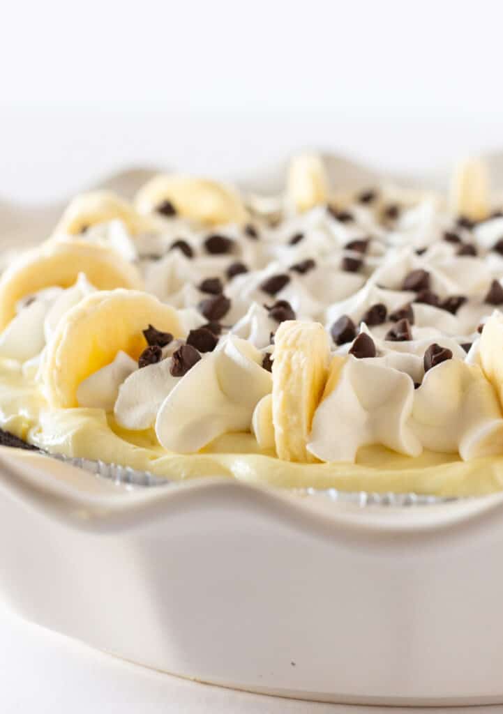 A chocolate banana cream pie topped with chocolate chips and whipped cream with sliced bananas around the perimeter.