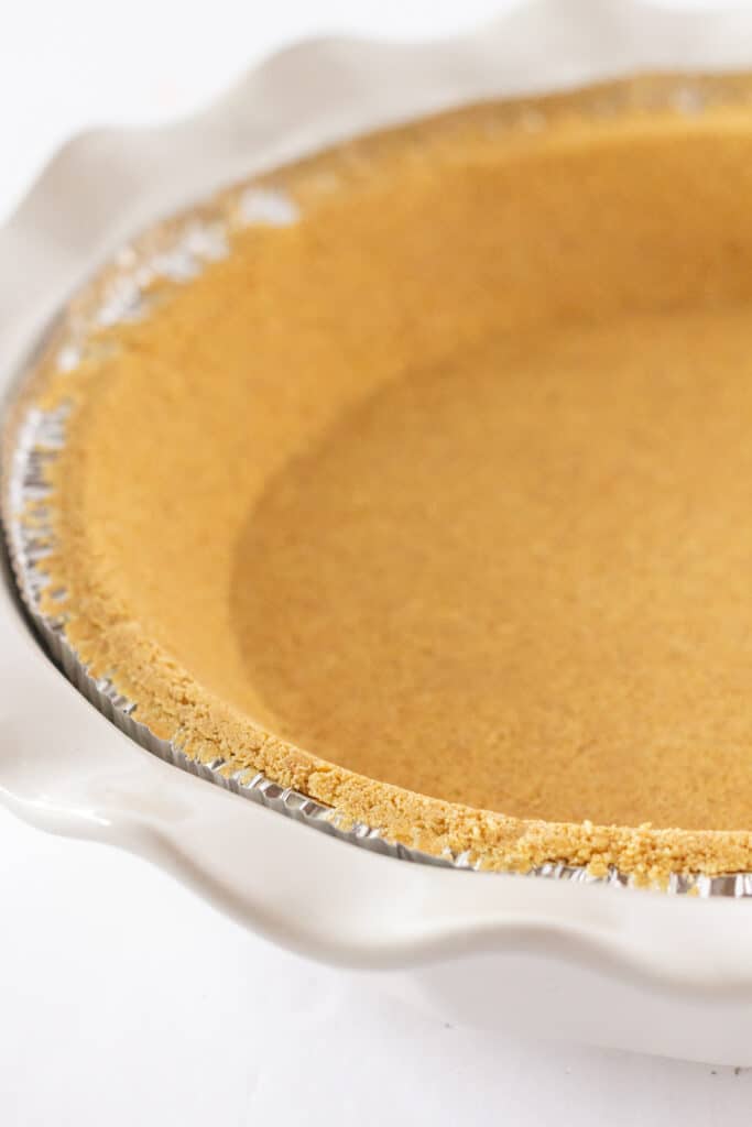 A graham cracker crust in a white baking dish.