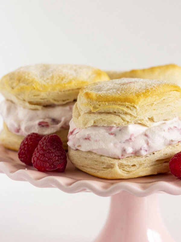 Raspberry shortcake on a pink cake plate with fresh raspberries.