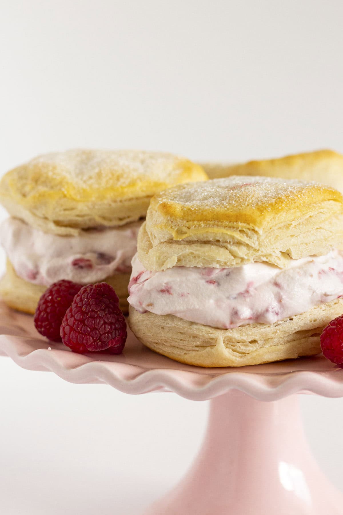 Raspberry shortcake on a pink cake plate with fresh raspberries.