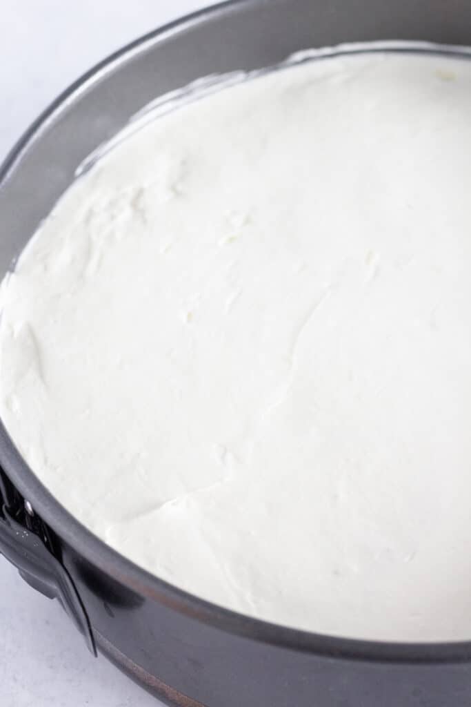 The white layer of the berry cheesecake spread over a raspberry layer in a springform pan.