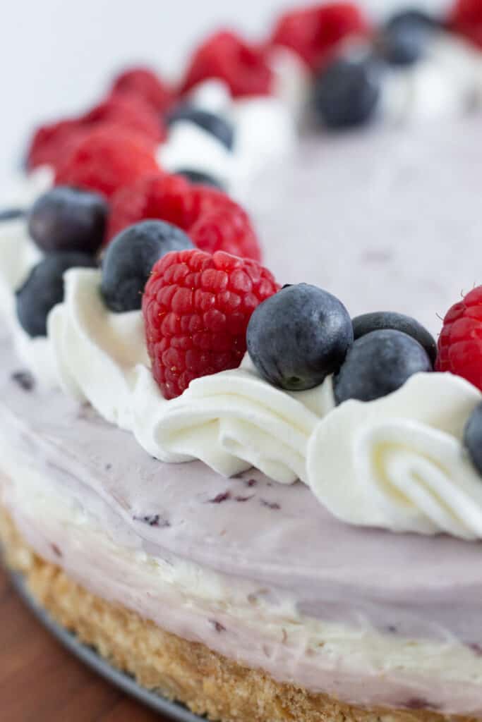 A completed no bake berry cheesecake topped with whipped cream and fresh fruit.