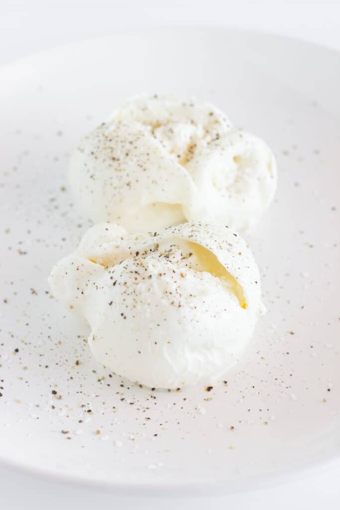 Burrata on a white platter, cut open and sprinkled with salt and pepper.