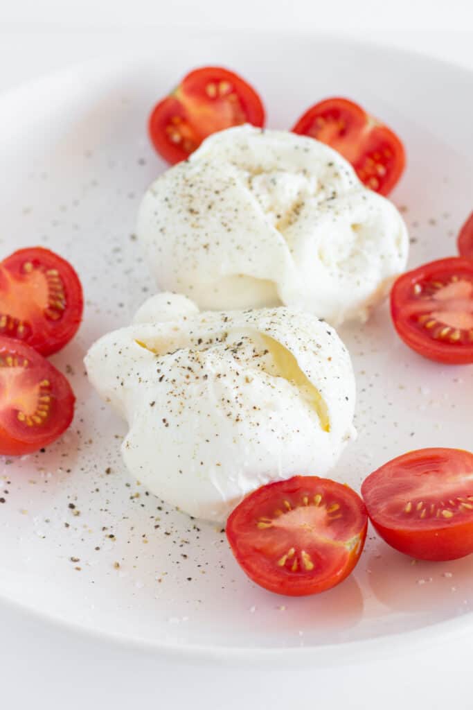 Burrata and halved cherry tomatoes on a white platter.