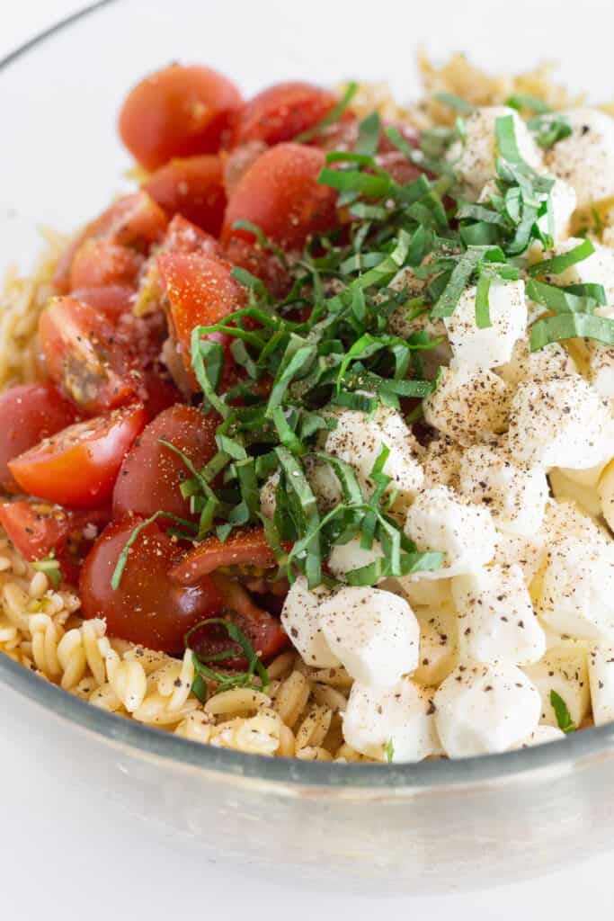 Orzo topped with halved cherry tomatoes, mozzarella pearls, seasoning, and slivered basil.