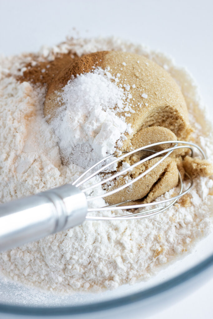 A whisk in a mixing bowl with the dry ingredients needed for this recipe for apple and blackberry crumble.