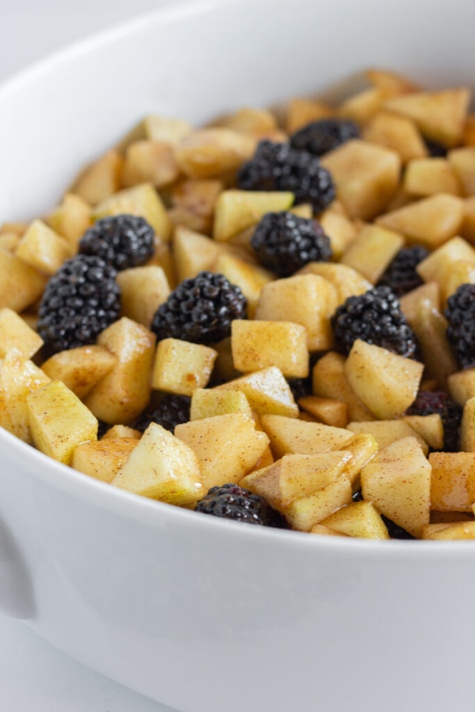 Unbaked apple blackberry crumble filling in a white baking dish.