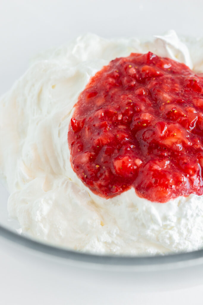 Whipped cream and fresh strawberry puree in a mixing bowl.