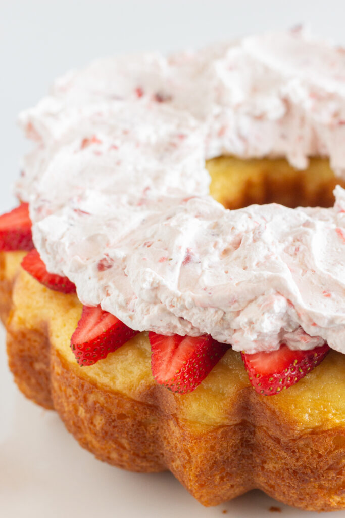 A vanilla pound cake topped with strawberry whipped cream and fresh strawberry.